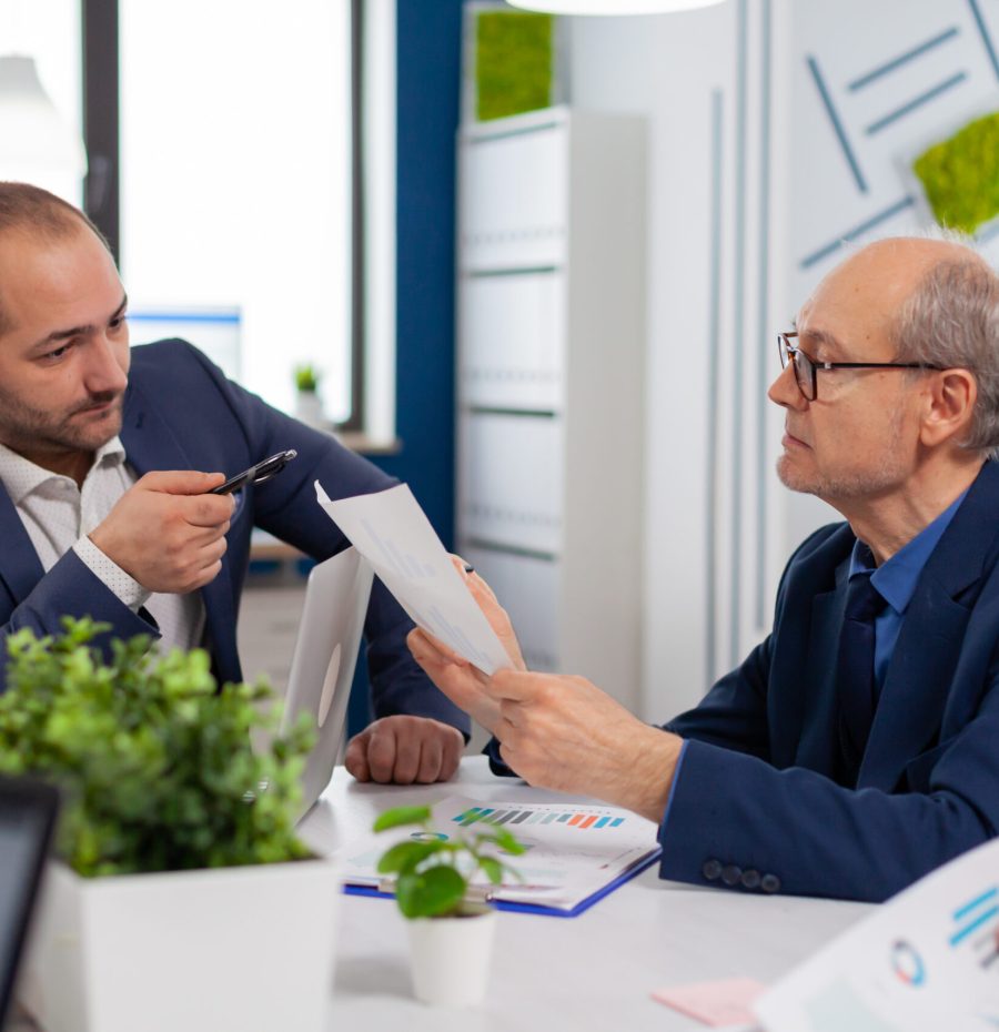 Senior entrepreneur discussing with coworker holding documents in conference during briefing Businessman discussing ideas with colleagues about financial strategy for new start up company.