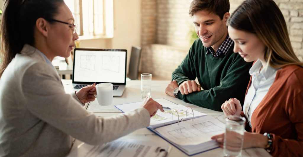 smiling-couple-insurance-agent-going-through-real-estate-plans-meeting-office-focus-is-man-min